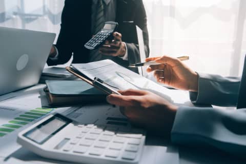 机の上で計算機と資料を使いながら話し合うビジネスマンたち。