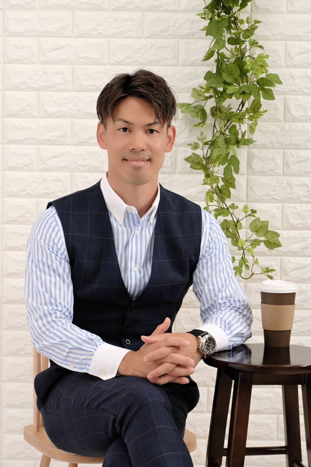 若い男性がスーツベストとストライプのシャツを着てカフェのテーブルに座っている。